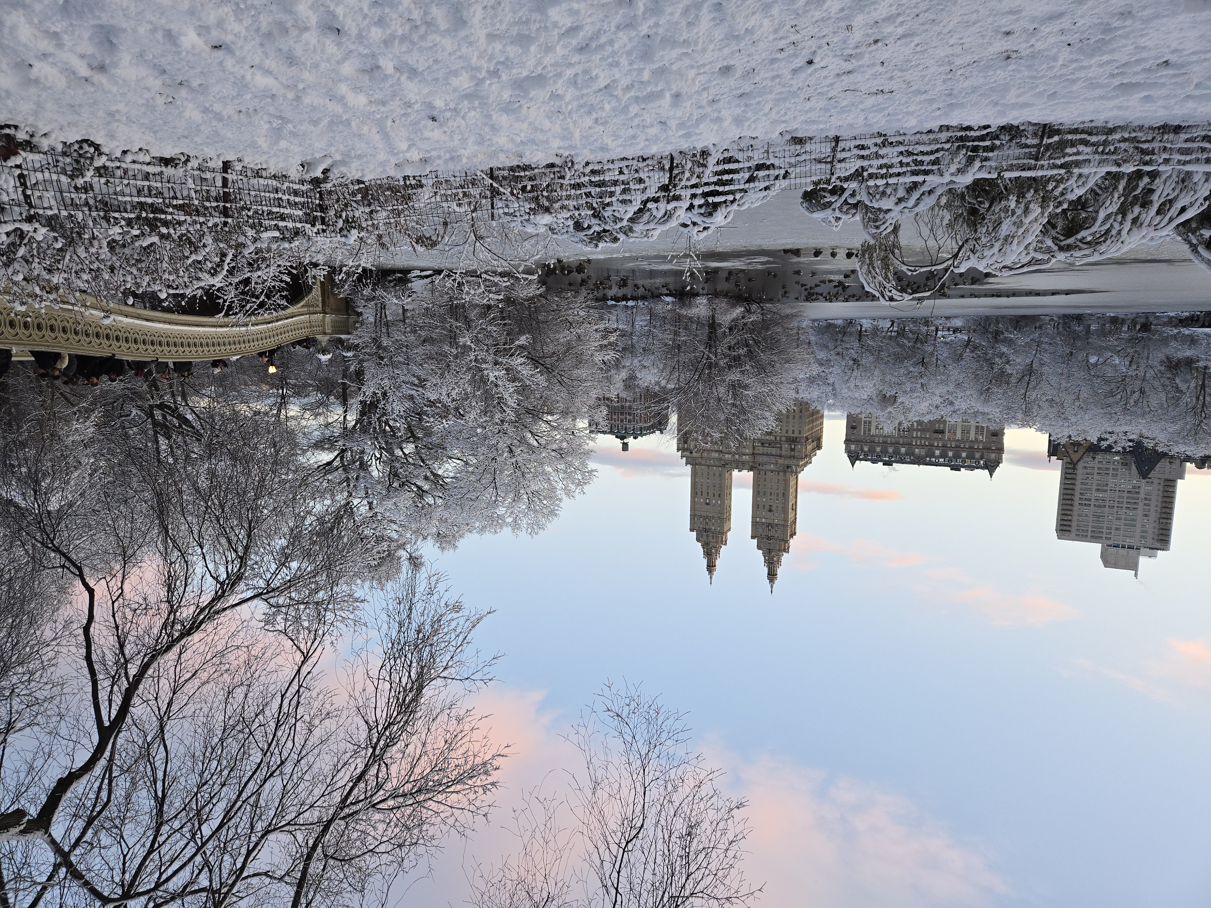 Central Park in winter — snow-covered trees, the Bow Bridge, and the San Remo towers at dusk